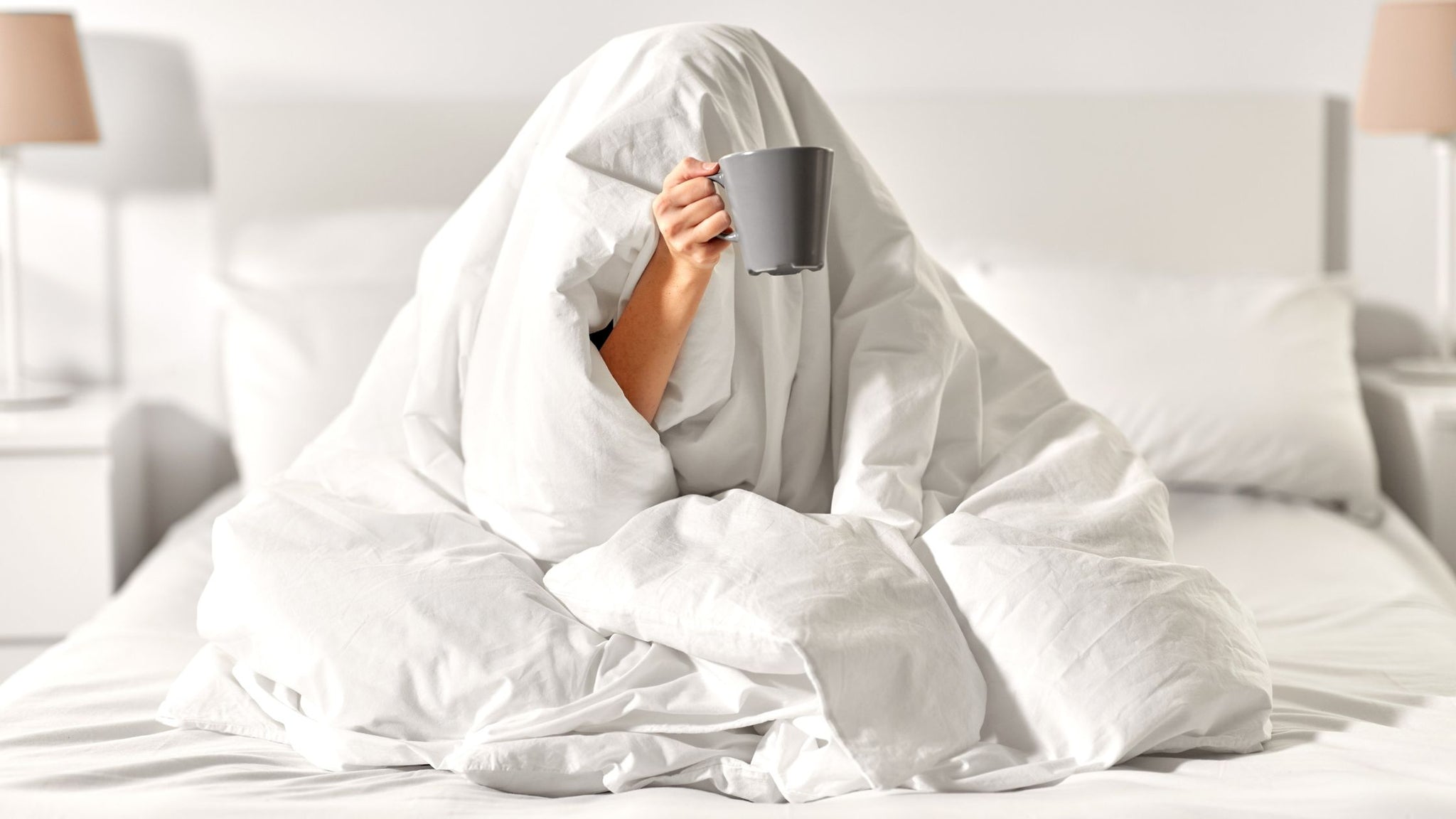 Woman in bed holding cup of CBT tea out the covers